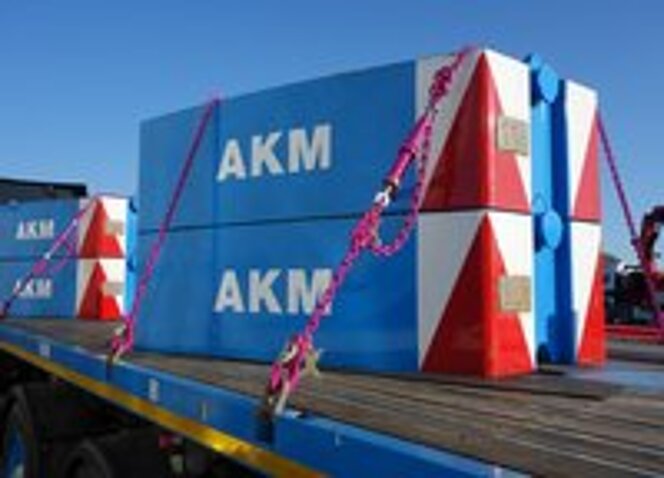 Ladungssicherung mit pinken RUD-Zurrketten am blauen AKM-Gewicht auf einem Lkw-Anhänger.