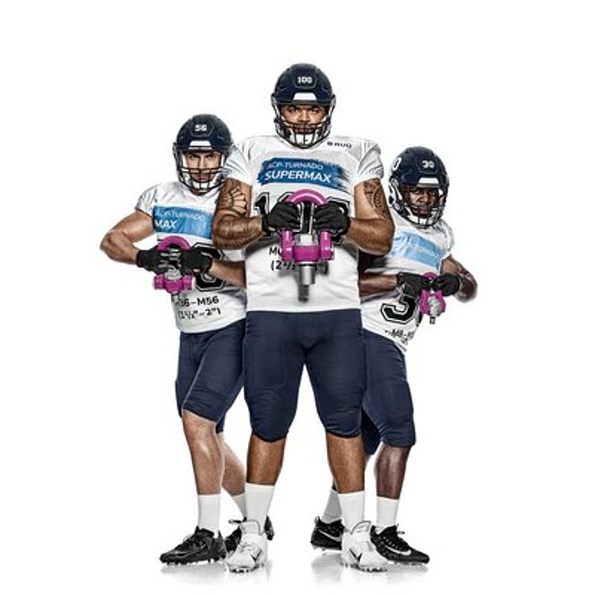Drei American Football-Spieler in Ausrüstung posieren kraftvoll nebeneinander. Sie tragen weiße Trikots mit der Aufschrift „ACP-TURNADO SUPERMAX“ und präsentieren jeweils einen pinken RUD ACP-TURNADO Anschlagpunkt in den Händen.