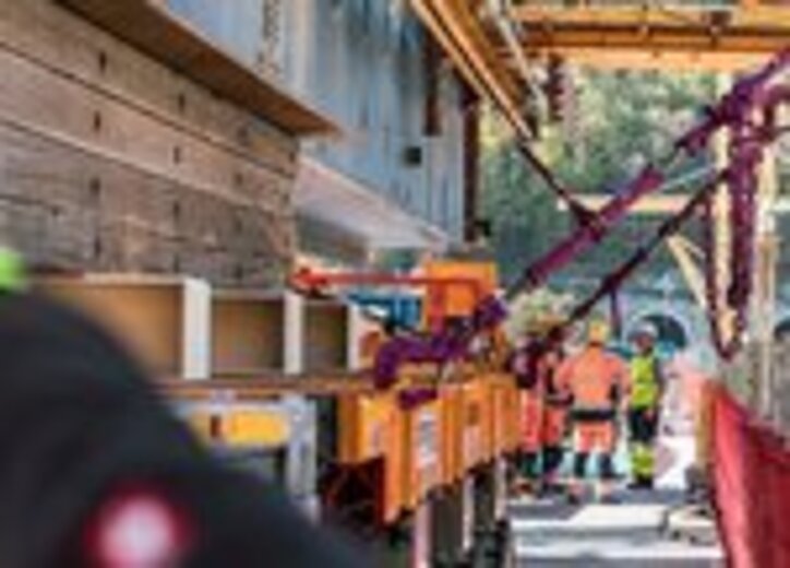 Bauarbeiter sichern mit RUD ICE-Zurrketten einen schweren Brückenträger auf einem Transportwagen während der Baustellenmontage.