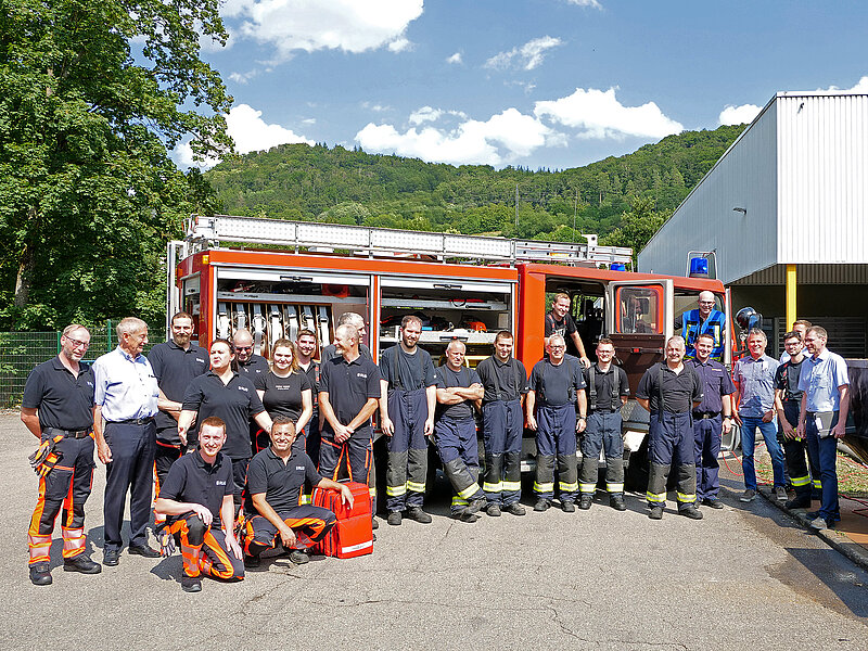 Eine große Gruppe der RUD Werkfeuerwehr steht gemeinsam vor einem Feuerwehrauto für ein Gruppenfoto.