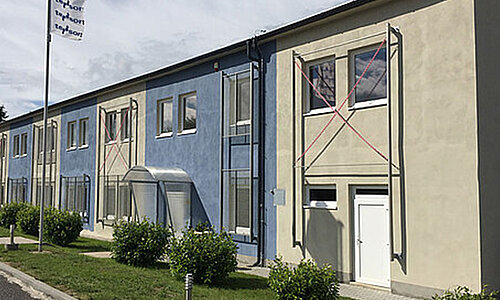 Firmengebäude von Tesort spol. s.r.o. mit blauer und beiger Fassade, davor Fahnenmast mit Firmenflagge.
