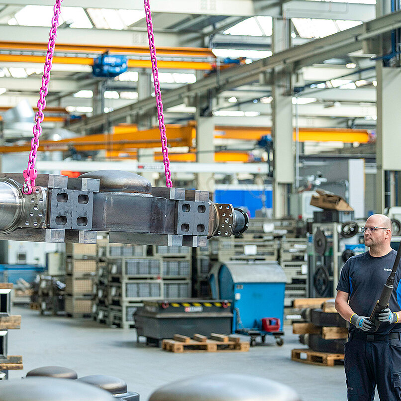Schweres Maschinenteil wird mit pinker Anschlagkette in einer Produktionshalle bewegt.