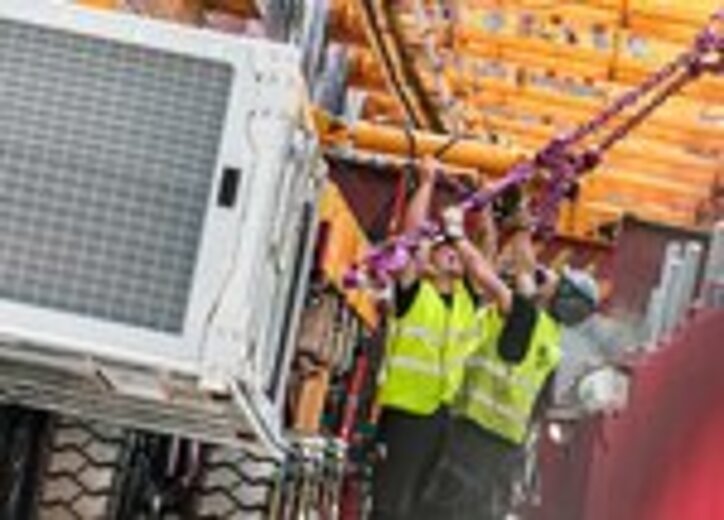 Zwei Arbeiter sichern mit einer RUD ICE-Zurrkette ein schweres Bauteil an einem Montagegerät auf der Baustelle.