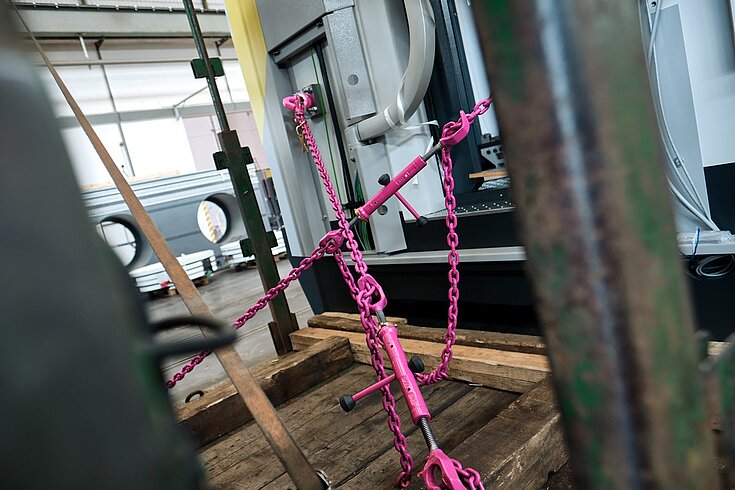 RUD-Zurrketten in Pink sichern eine Maschine auf Holzpaletten während des innerbetrieblichen Transports.