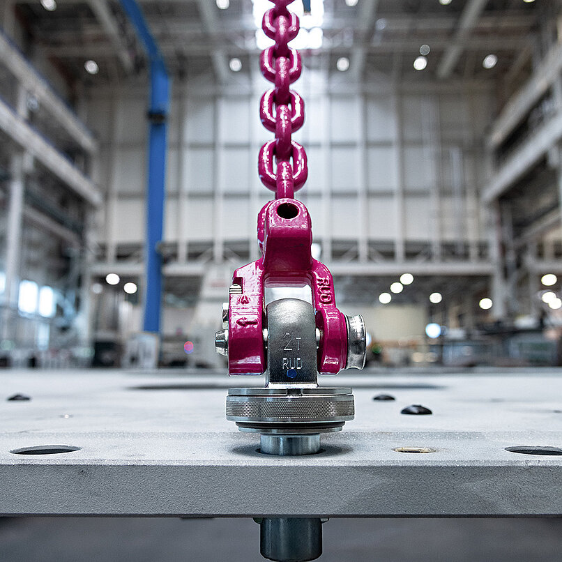 CCS-FastLox Anschlagpunkt mit pinker Kette an einer Stahlplatte in Industriehalle befestigt.