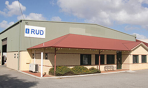 RUD Chains Pty Ltd Standort Australien, flaches Bürogebäude mit rotem Dach und angrenzender Industriehalle mit großem RUD Logo.
