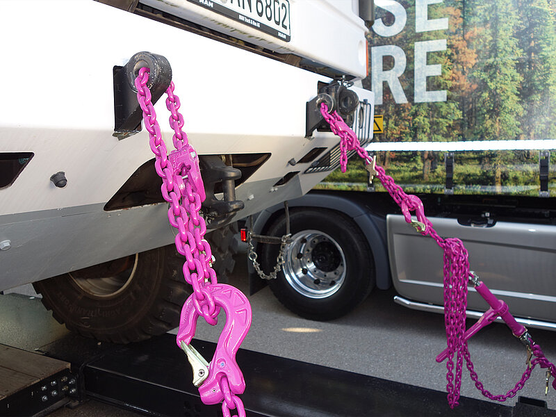 RUD Kranzketten in Pink sichern ein Fahrzeug auf einem Anhänger für den sicheren Transport.