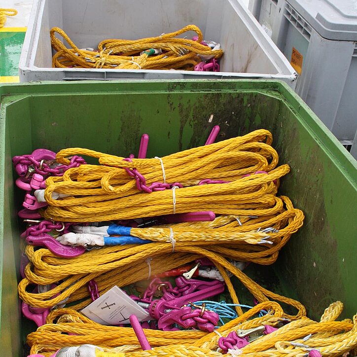 Gelbe RUD-Faserseile mit lila Ketten und Haken sauber in Behältern für den Transport gelagert.
