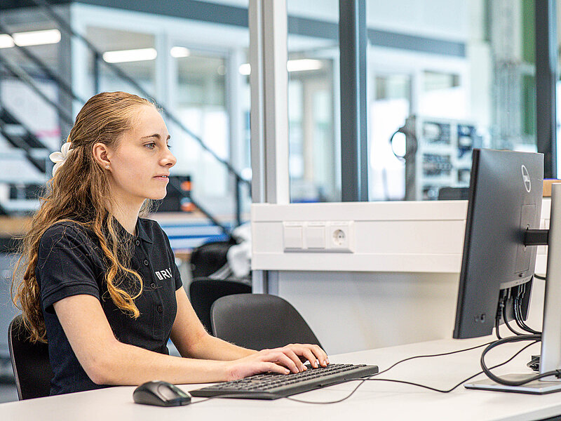 Eine junge RUD Mitarbeiterin sitzt im Büro an einem Schreibtisch und arbeitet konzentriert am Computer.