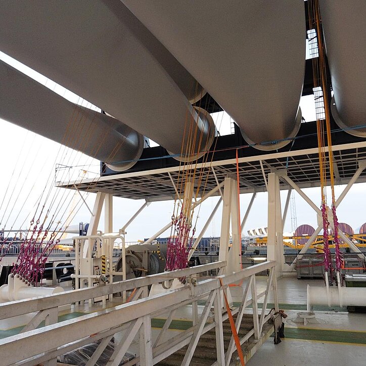Transport von Windkraftflügeln auf einem Spezialschiff, gesichert mit gelben Faserseilen und RUD-Ketten.
