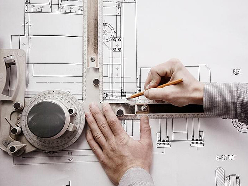 Eine Person fertigt mithilfe eines technischen Zeicheninstruments eine präzise Konstruktionszeichnung auf Papier an.