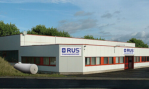 Außenansicht des RUS Zerspanungstechnik GmbH Gebäudes mit weißer Fassade und Firmenlogo.