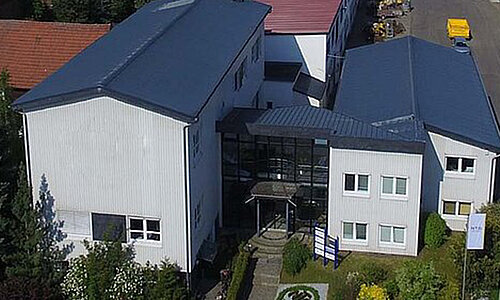 Luftaufnahme des RUD System GmbH Standorts mit modernem weißen Bürogebäude und Firmenflaggen.