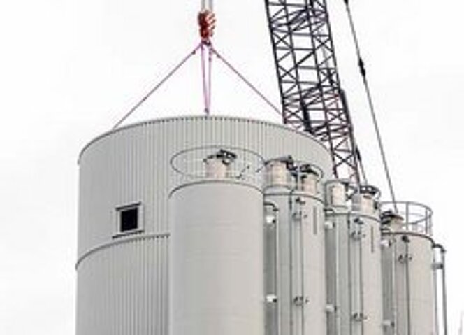 Ein Kran hebt unter Verwendung von RUD ICE-2-Strang-Gehängen den oberen Teil eines großen Betonsilos zur Montage neben bereits installierten Siloeinheiten an.