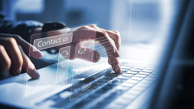 Finger tippt auf Laptop-Tastatur, überlagert von digitaler Benutzeroberfläche mit Kontaktoptionen wie Chatbot, Telefon, E-Mail und Chatfenster.