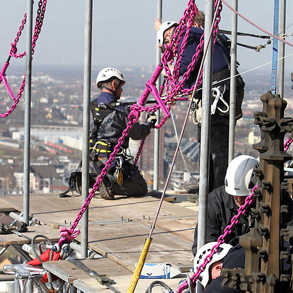 Arbeiter sichern in hoher Höhe ein Hängegerüst am Kölner Dom mit RUD ICE-1-Strang-Gehängen.