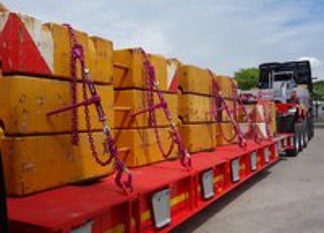 Schwerlastladung mit gelben Gegengewichten, gesichert mit pinkfarbenen RUD-Zurrketten auf rotem Tieflader.