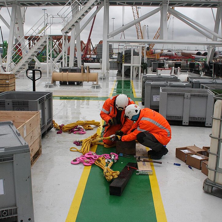 Monteure auf Offshore-Schiff prüfen pinke RUD-Hebepunkte und gelbe Anschlagmittel.