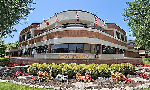 Außenansicht des Caldwell Firmengebäudes in den USA mit Flaggen und gepflegter Gartenanlage.