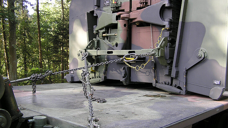 Schweres militärisches Gerät wird mit Ketten und Spannsystemen auf einem Transportfahrzeug gesichert.