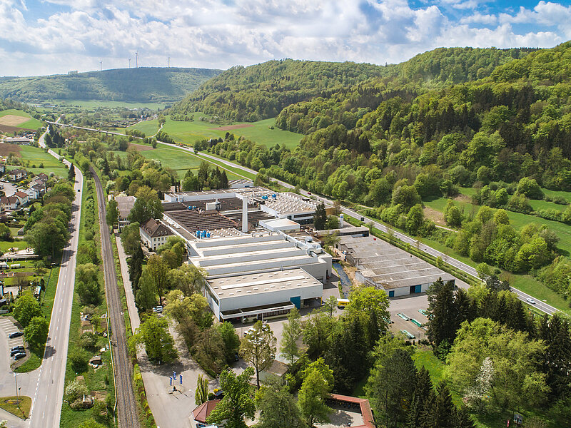 Luftaufnahme des RUD-Werks in Unterkochen, umgeben von Straßen, Bahnstrecke und grünen Hügeln.