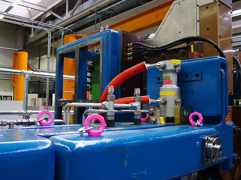 Industrielle Fertigungsanlage mit Hydrauliksystemen und farblich markierten Sicherheitsvorrichtungen.