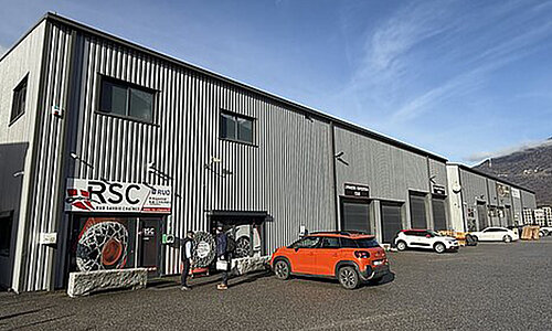 Außenansicht des RSC SARL Gebäudes mit RUD Snow Chains Logo und geparkten Autos.