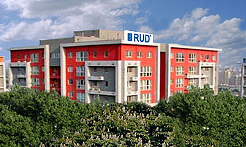 RUD Rieger & Dietz Beijing Trading Ltd, mehrstöckiges Bürogebäude in Rot und Grau mit RUD Logo auf dem Dach, umgeben von Bäumen.
