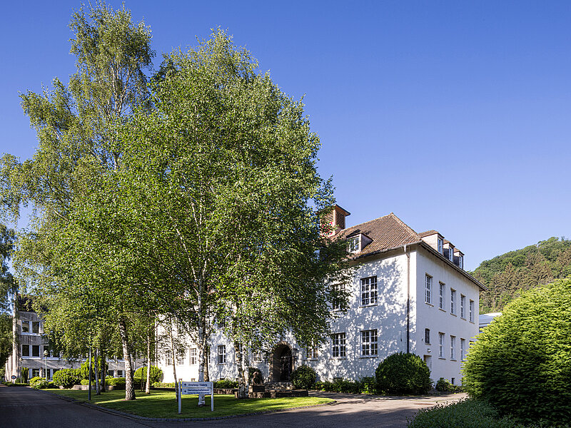 Weißes Gebäude des RUD-Schulungszentrums, umgeben von Bäumen und Grünflächen bei klarem Himmel.