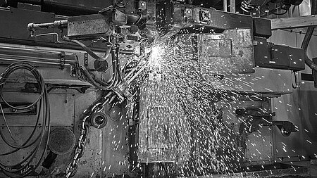 Historisches Foto einer Maschine bei der elektrischen Schweißung von Kettengliedern mit sichtbarem Funkenflug.