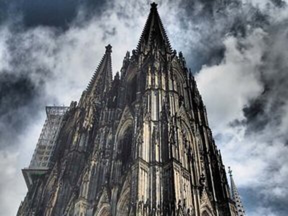 Frontansicht des Kölner Doms mit einem großen Hängegerüst an der Spitze des Nordturms für Restaurierungsarbeiten.