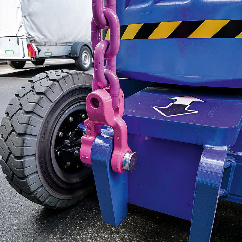 Anschlagkette mit pinkem Verbindungsglied an einem Fahrzeugrahmen mit Pfeilmarkierung.