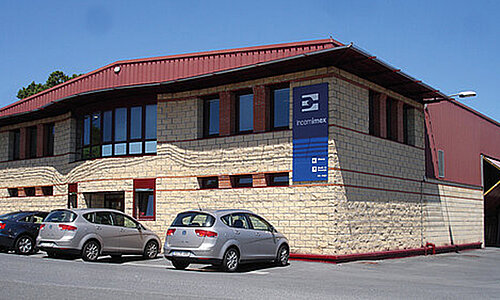 Firmengebäude von Incomimex S.L. mit Firmenlogo an der Fassade und geparkten Autos davor.