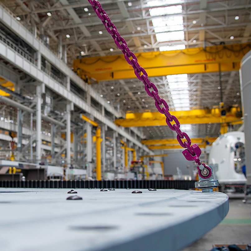 RUD-Anschlagkette mit pinkem Haken an einer großen Stahlplatte in Industriehalle befestigt.