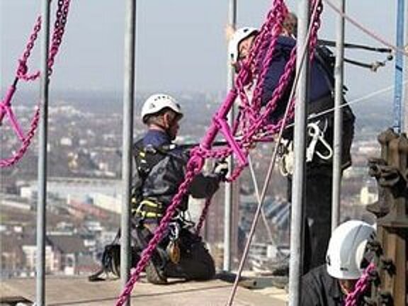 Arbeiter sichern in hoher Höhe ein Hängegerüst am Kölner Dom mit RUD ICE-1-Strang-Gehängen.