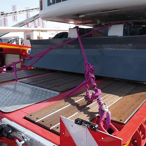 RUD ICE Güteklasse‑12 Zurrketten mit Spannelement sichern eine Baumaschine auf dem Tiefbettauflieger.