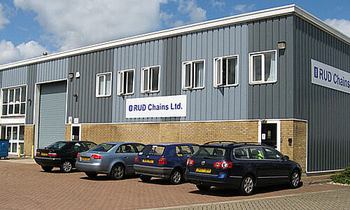 Außenansicht des RUD Chains Ltd. Gebäudes mit grauer Fassade, Firmenlogo und geparkten Autos.