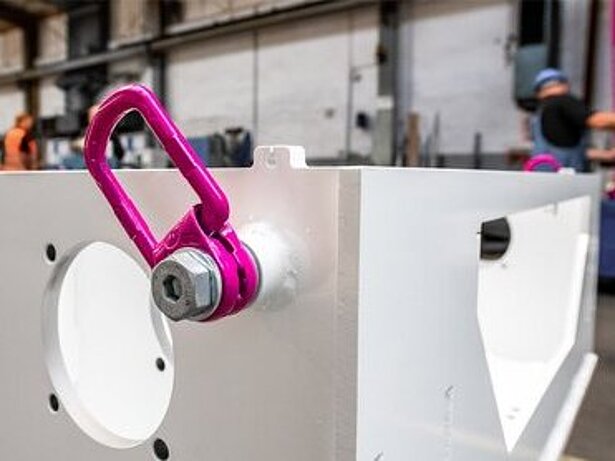 Ein RUD Anschlagpunkt VLBG-PLUS ist an einem hellen Metallbauteil in einer Industriehalle montiert.