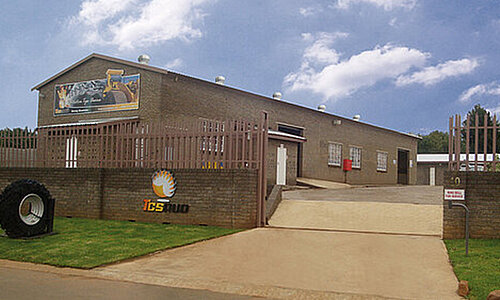 TCS RUD Standort mit Backsteingebäude, Einfahrtstor und großem Reifenmodell im Vorgarten.