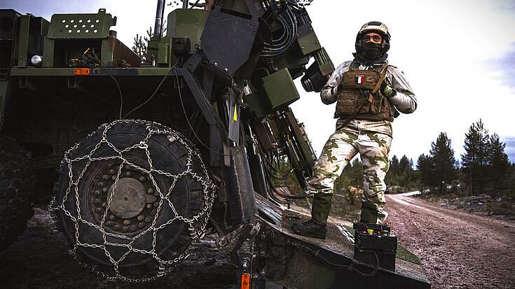 Soldat neben Militärfahrzeug mit montierten RUD Gleitschutzketten im winterlichen Gelände.