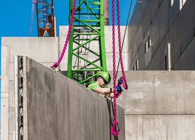 Ein Bauarbeiter befestigt RUD ICE-Kettengehänge an einem schweren Betonfertigteil auf der Baustelle der Papierfabrik Palm in Aalen.
