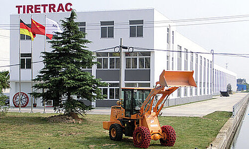 Außenansicht des Tiretrac Standorts mit Firmengebäude, Flaggen und Radlader mit Spezialketten.