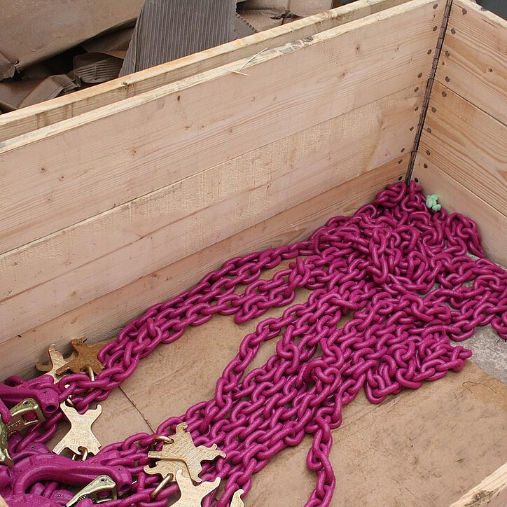 Lila RUD-Hebeketten mit Haken liegen ordentlich in einer Holzkiste bereit für den Einsatz.