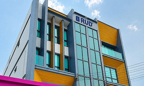 RUD Lifting (Thailand) Co., Ltd., modernes mehrstöckiges Bürogebäude mit gelben Fassadenelementen und auffälligem pinkem Vordach.
