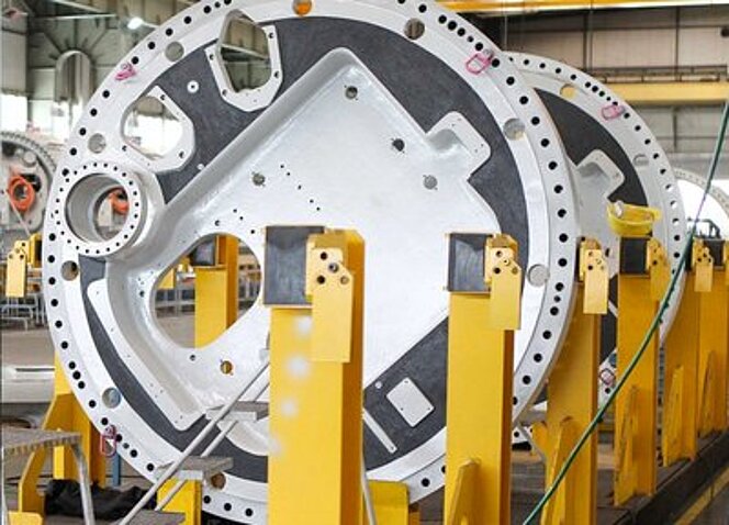 Große Gussteile für Windkraftanlagen mit montierten RUD Anschlagpunkten stehen in einer Fertigungshalle auf gelben Halterungen.