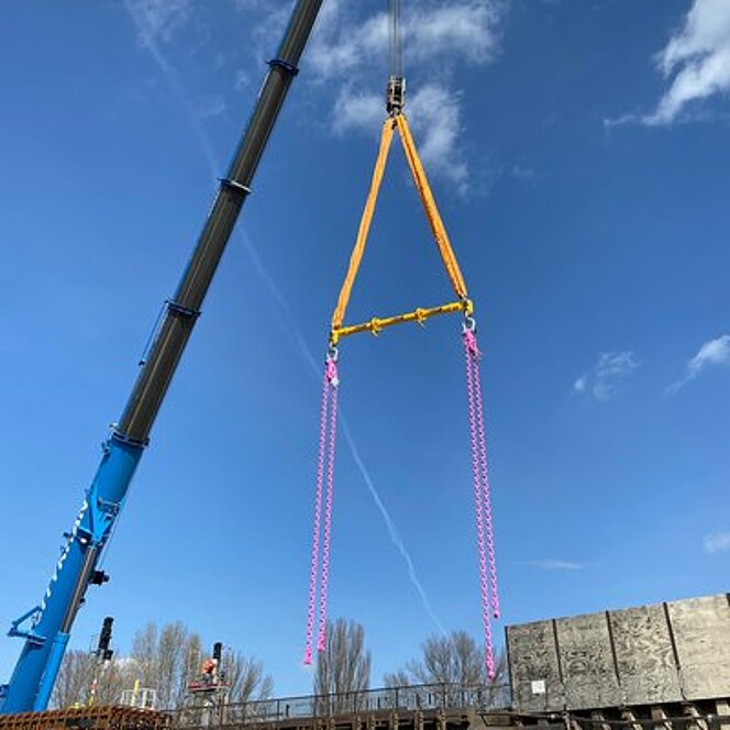 Zwei pinke RUD ChainBlocks mit gelbem Spreizträger hängen am Kran auf einer Baustelle.