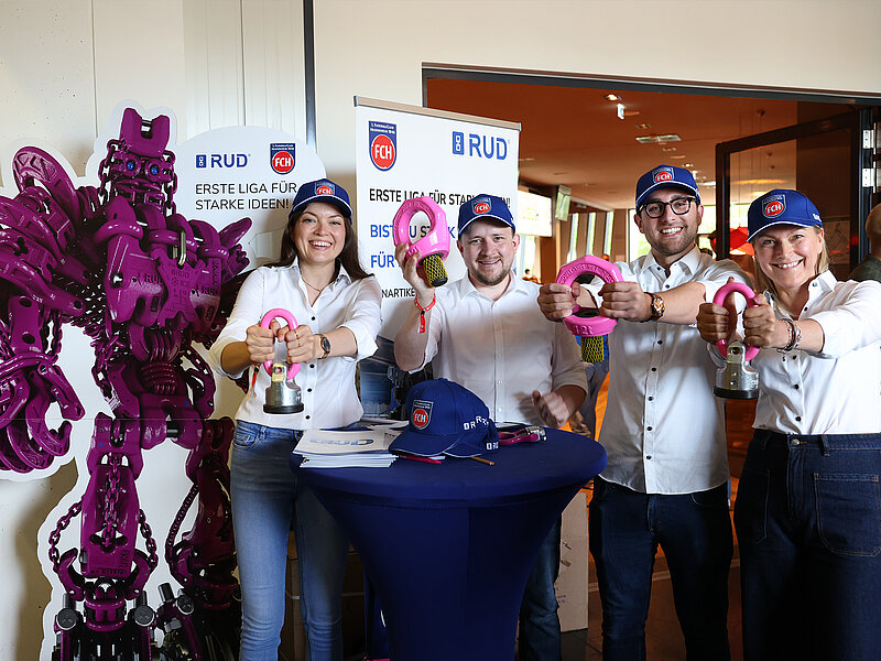 RUD-Teammitglieder mit FCH-Kappen präsentieren pinke Anschlagpunkte bei einer Sponsoring-Aktion.