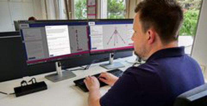 Mitarbeiter am Schreibtisch nutzt RUD Anschlagmittel-Konfigurator an zwei Monitoren.