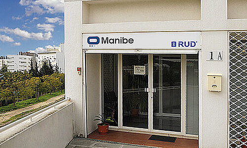 Eingangsbereich des Firmengebäudes von RUD Manibe Tecnologia Industrial Lda mit Firmenlogo über der Tür.