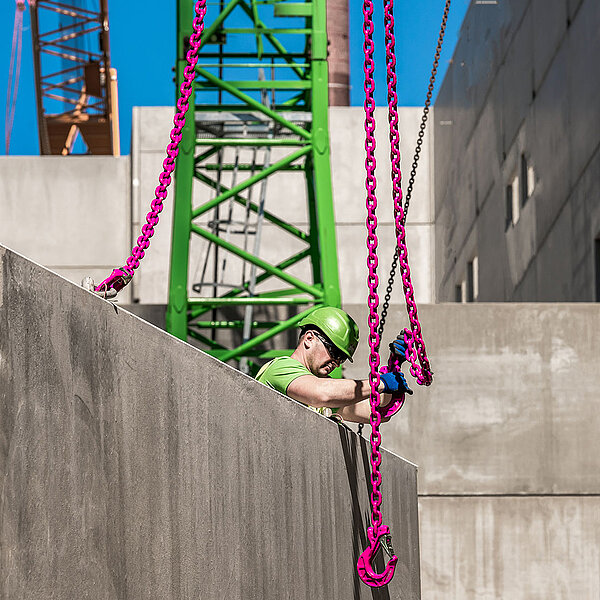 Ein Bauarbeiter befestigt RUD ICE-Kettengehänge an einem schweren Betonfertigteil auf der Baustelle der Papierfabrik Palm in Aalen.